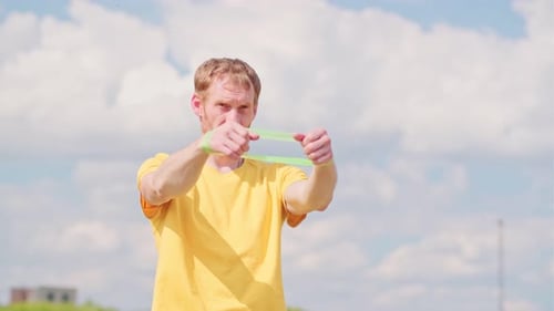 Um esportista profissional com uma camisa amarela está segurando um expansor de elástico. Ele parece focado e