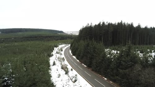 Snowy curved winter woodland road aerial tracking forward view following forest tree landscape