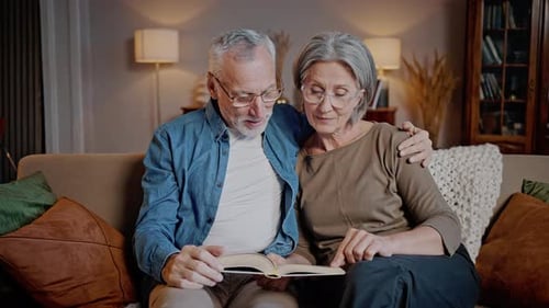 Elderly Man and Woman Read Book Together Sitting at Home