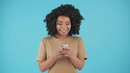 Woman Smiling and Using Smartphone on Blue Backdrop