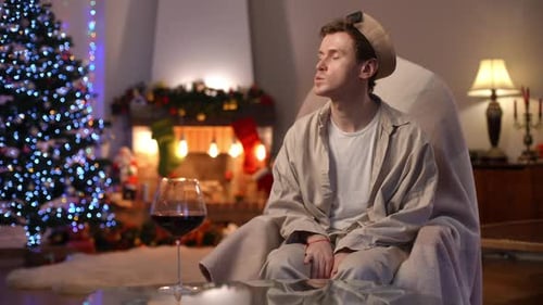 Depressed Young Man Looking Away Sighing Putting Chin on Hands Sitting in Rocking Chair in Living