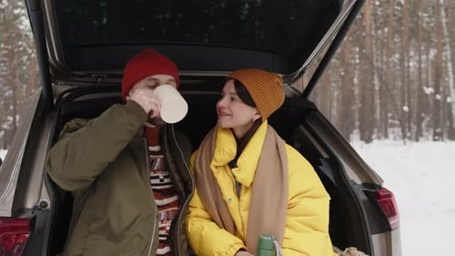 Portrait of Couple Enjoying Warm Drink and Smiling for Camera In Winter Forest