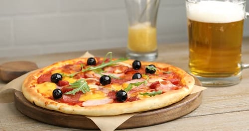Pouring beer into glass on wooden table, focus on tasty pizza