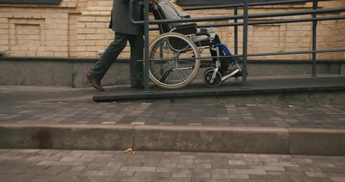 Man Pushing Wheelchair Along City Sidewalk