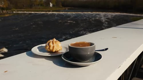 Tableware with a Coffee Cup and Pastry By a River
