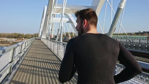 Male runner running on the bridge in the city during day.