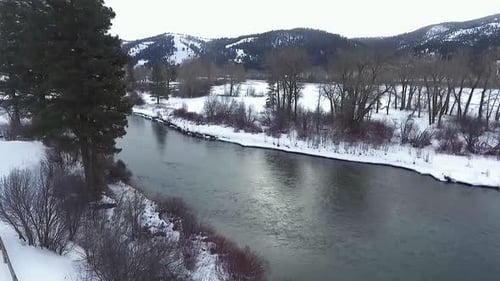 AERIAL - Camera bends around tree revealing a beautiful snowy river