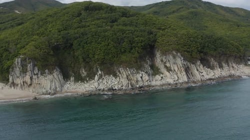 Vogelperspektive einer steilen Klippe am Meer mit grünen Waldhügeln auf der Spitze. Aufnahme aus der Luft