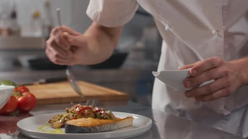 Chef Adding Sauce to Salmon Dish in Kitchen