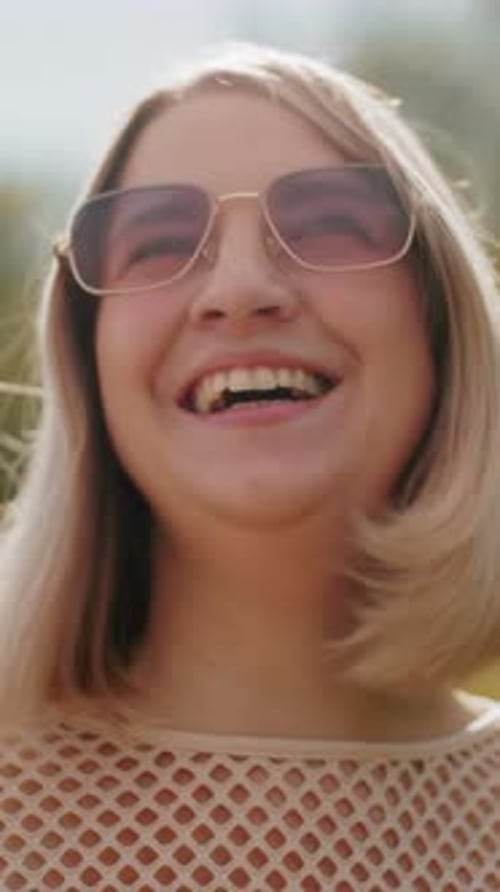 Femme d'affaires souriante en lunettes de soleil sous un ciel ensoleillé avec fond de verdure
