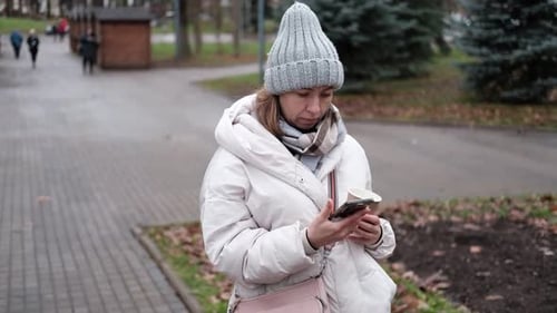 Portrait of Mature Woman in Wool Hat Standing on the Urban Street with Mobile Phone in Hand
