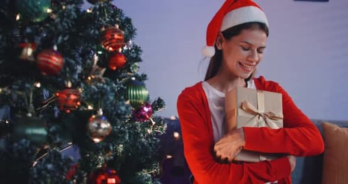 Smiling Woman Holds Christmas Gift Near Tree