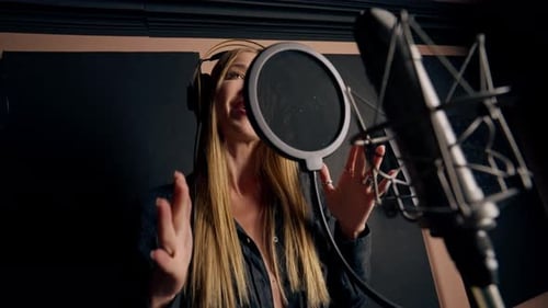 girl singer singing in a recording studio with headphones in front of microphone to create a song
