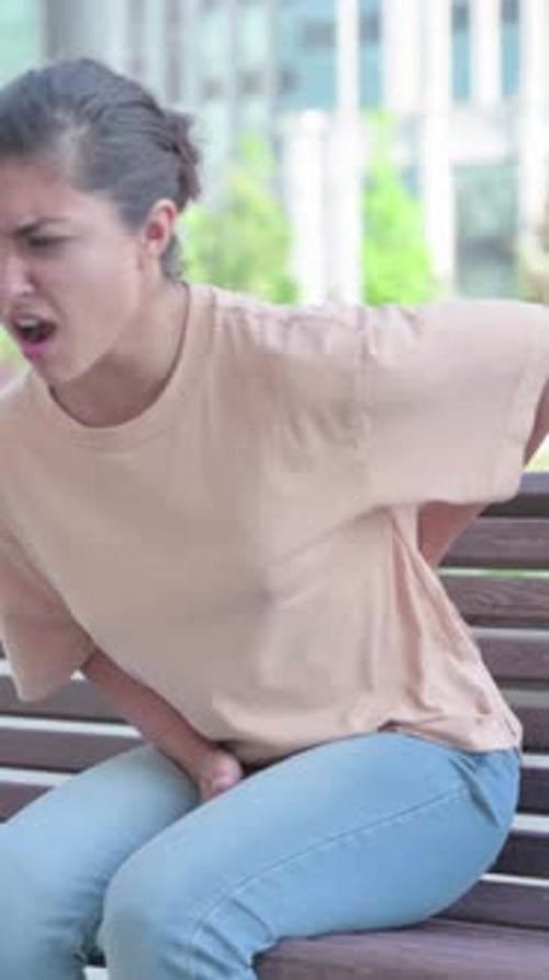 Woman on Bench Experiences Back Pain in the City