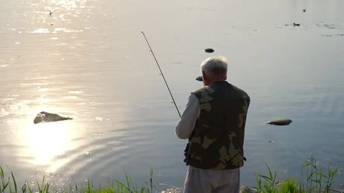 Velho pescador sênior de cabelos grisalhos lança um giro da costa ao pôr do sol torcendo um