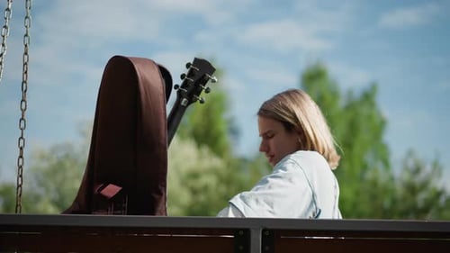 Teen Putting Guitar in Case on Park Bench