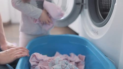 Junge Tochter hilft Mama freudig dabei, frische Wäsche aus der Waschmaschine zu entladen