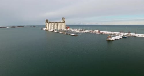 Drone flying over a harbor towards an old industrial building on the lakeshore of Georgian Bay.