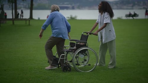 A Caring Caregiver Helps an Elderly Person in a Wheelchair Enjoy Nature in a Beautiful Park