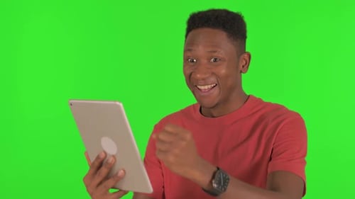Casual African Man Celebrating Success on Tablet on Green Background