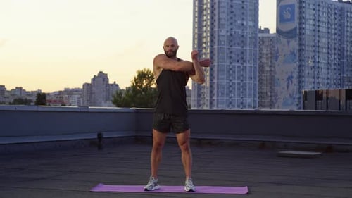 An Athletic Man Begins His Evening Workout on the Rooftop of a Big City
