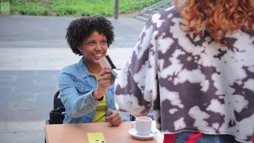Woman Happily Paying with Credit Card While Seated at a Table in a Lively Outdoor Cafe Atmosphere