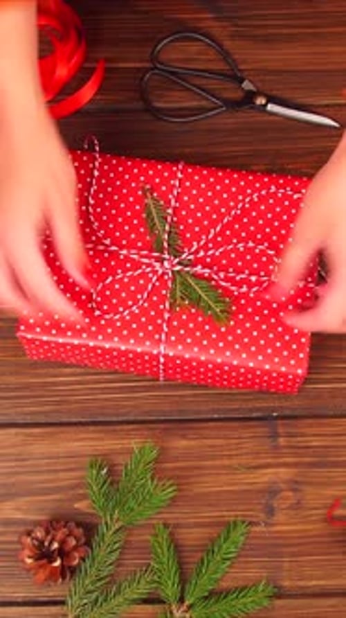 Vertical Video of Woman Wrapping Gift Box with Decorating Items on Wood Table Close Up Top View