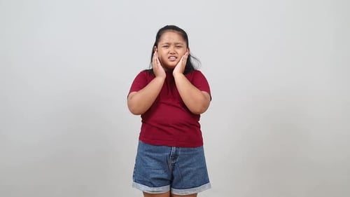 Sick ill sad Asian little girl touching cheek suffering from toothache, isolated on white