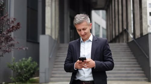 Happy Businessman Smiling While Using Phone Outside Office