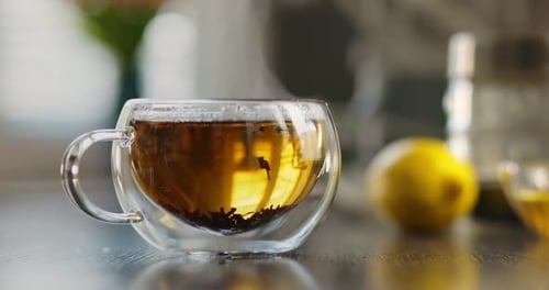 Heißer Tee in einer Glastasse mit Rauch auf einem Holztisch in der Küche