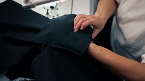 Nahaufnahme einer alten Näherin, die mit einer Nadel auf schwarzem Stoff arbeitet, handgemacht