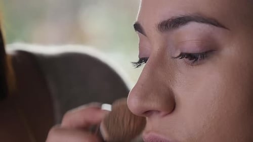 A professional make-up artist applies a make-up base to a female model's face.