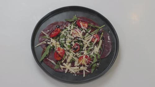 A chef preparing a fresh salad made of prosciutto, tomatoes, greens, and cheese, artfully combining