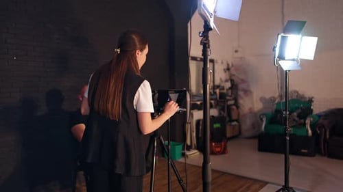 Woman Adjusting Camera in Studio, Man Sits