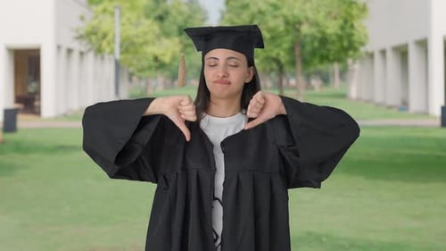 Disappointed Indian college graduate girl showing thumbs down sign