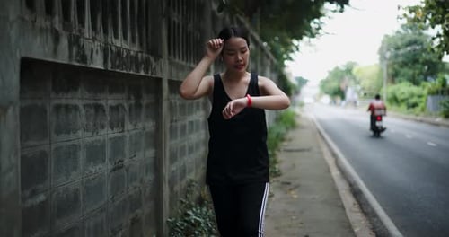 A young woman walks for exercise, enjoying the nice atmosphere on the sidewalk.