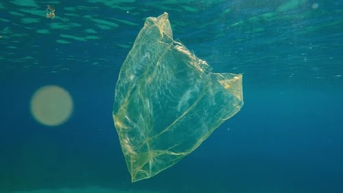 Una vieja bolsa de plástico amarilla flotando bajo el agua reflejada en la superficie a la luz del sol