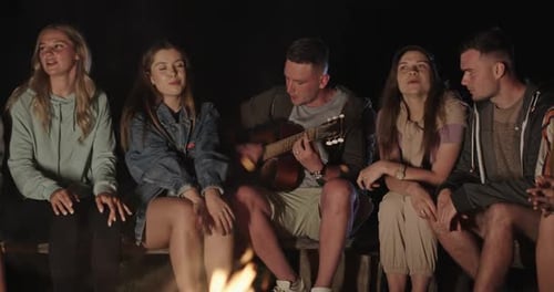Friends Singing Around Campfire with Guitar at Night