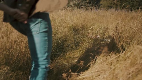 A man and a woman are running through a grass field toward a picnic blanket.