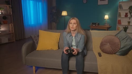 A Woman Plays a Consular Game with a Game Controller While Sitting on the Couch at Home in the