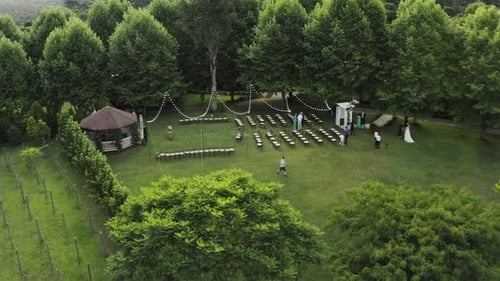 Drone flying away from wedding venue in a green field under the tree with lights. Tradition outdoor