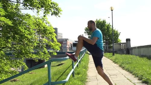 Handsome young man jogger stretching legs in city park super slow motion
