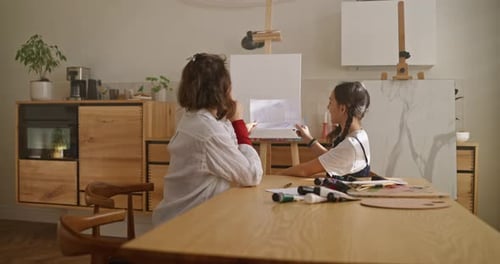 Happy Little Girl with Her Mom Inspecting Her Drawings While Doing a Hobby at the Table in a Sunny