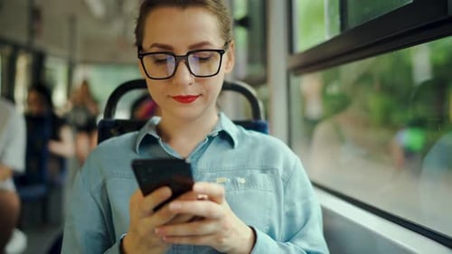 Woman With Glasses Rides Bus Looking at Phone