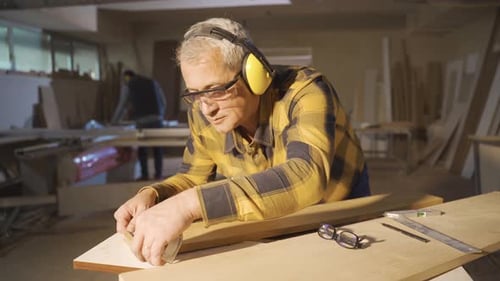 An adult carpenter works in a carpentry shop.
