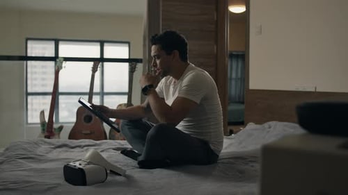 Man Sits on Bed Using Tablet Device