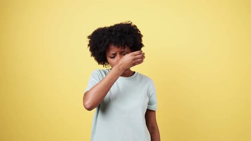 Junge Frau niest auf gelbem Hintergrund