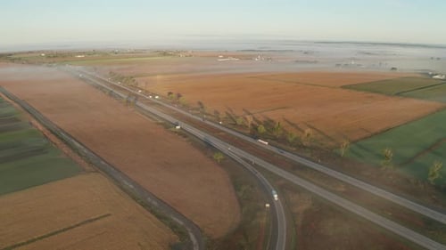 Morning fog over rural landscape and highway with cars and trucks driving on road. Vehicles exit and