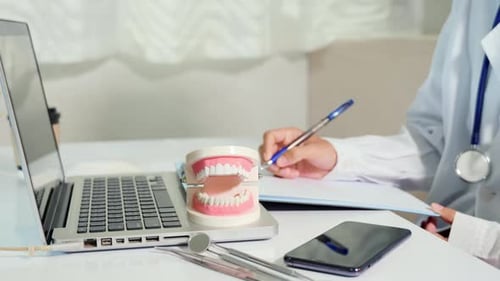 Dentist Writing Notes at Desk with Laptop
