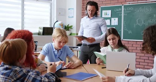 Enthusiastic Caucasian Teacher Showing Digital Tablet to Male and Female Pupils Sitting Together at